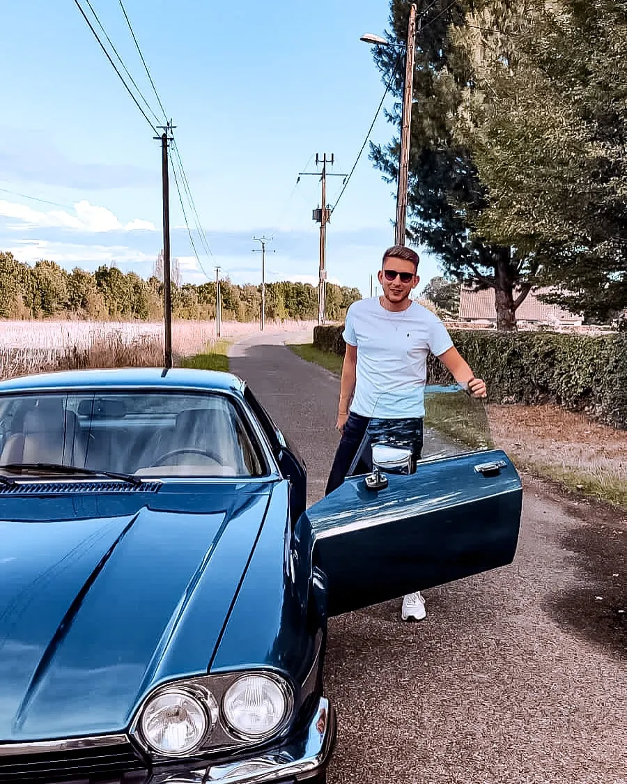 Charles Baras devant une Jaguar ancienne, sur une route de campagne
