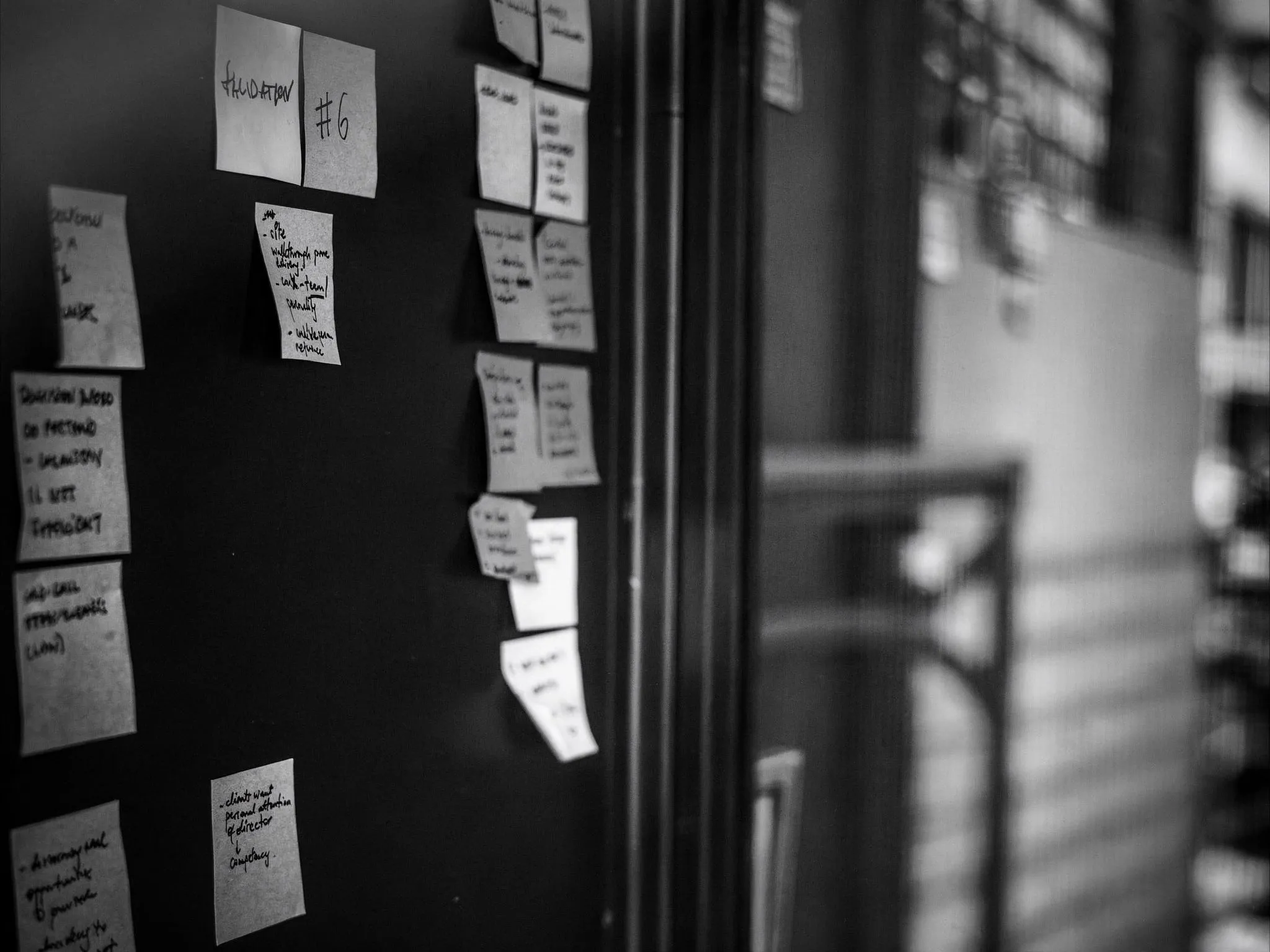 Mur de bureau couvert de post-it manuscrits, photographié en noir et blanc