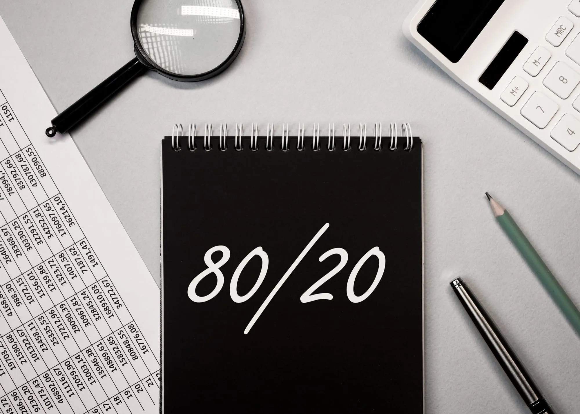 Bloc-notes noir portant « 80/20 », loupe, calculatrice et tableaux chiffrés autour