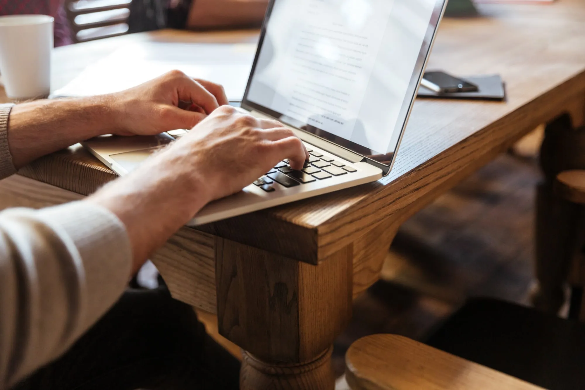 Mains d'un homme sur le clavier d'un portable, à une table en bois de café